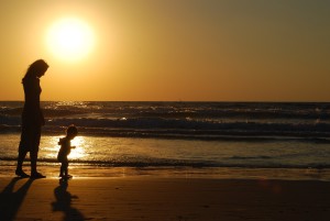 young woman with small child on the sea shore on sunset