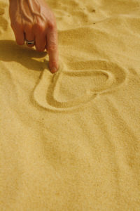 Hand drawing heart in sand on the beach